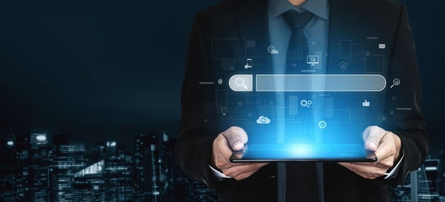 A person in a suit holds a glowing tablet with digital search icons projected above it, set against a dark cityscape.