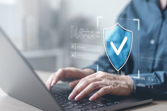 Hands typing on a laptop with a digital shield and checkmark