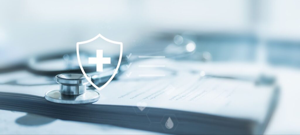 A stethoscope lies on medical documents, overlaid with a shield and cross icon