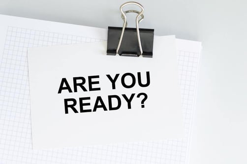 A paper clipped to a stack of graph paper with the bold question "ARE YOU READY?" printed on it, symbolizing preparation and readiness.