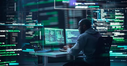 IT professional working on multiple monitors surrounded by code, symbolizing advanced cybersecurity and operating system layer protection with IGEL OS.