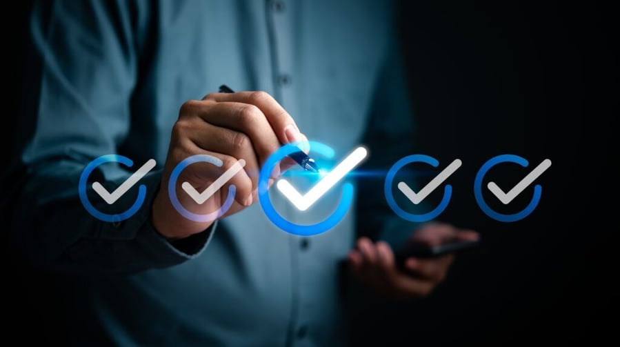 A person in a blue shirt holds a phone and uses a stylus on a glowing checkmark among a row of faded ones