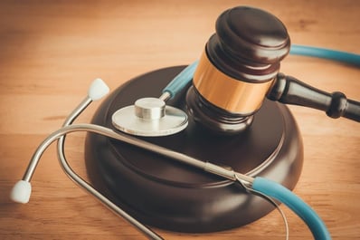 Gavel and stethoscope on a wooden table representing legal compliance in healthcare and regulated industries.