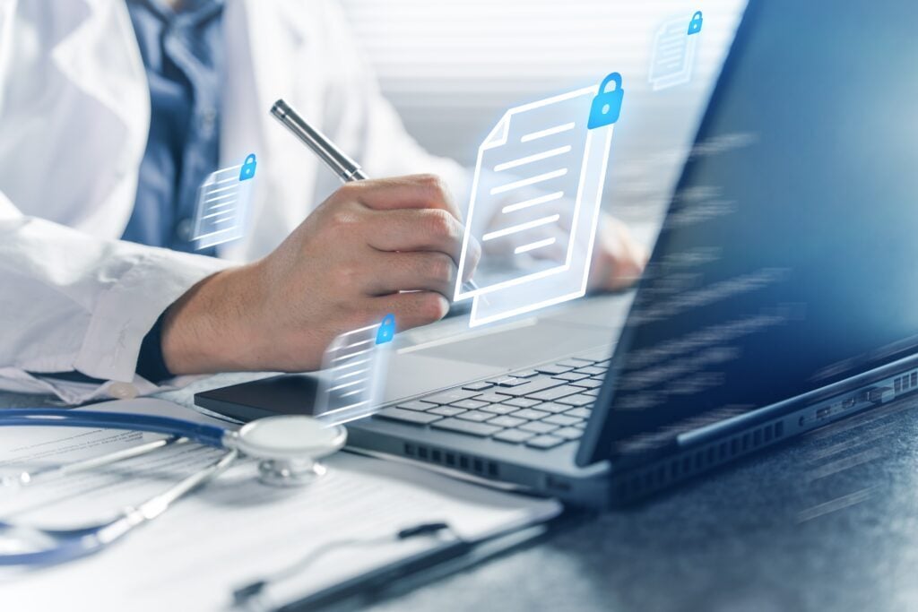 A person in a white coat writes on a clipboard near a laptop, with digital document icons floating, signifying secure digital healthcare management